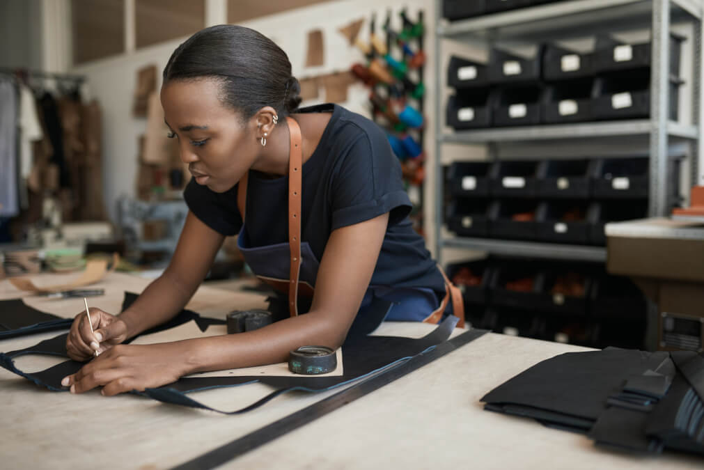 African,Female,Artisan,Using,A,Pattern,On,Leather,In,Her